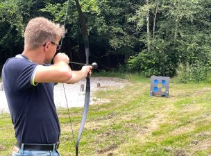 een foto waarop boogschieten als onderdeel van een zeskamp wordt getoont